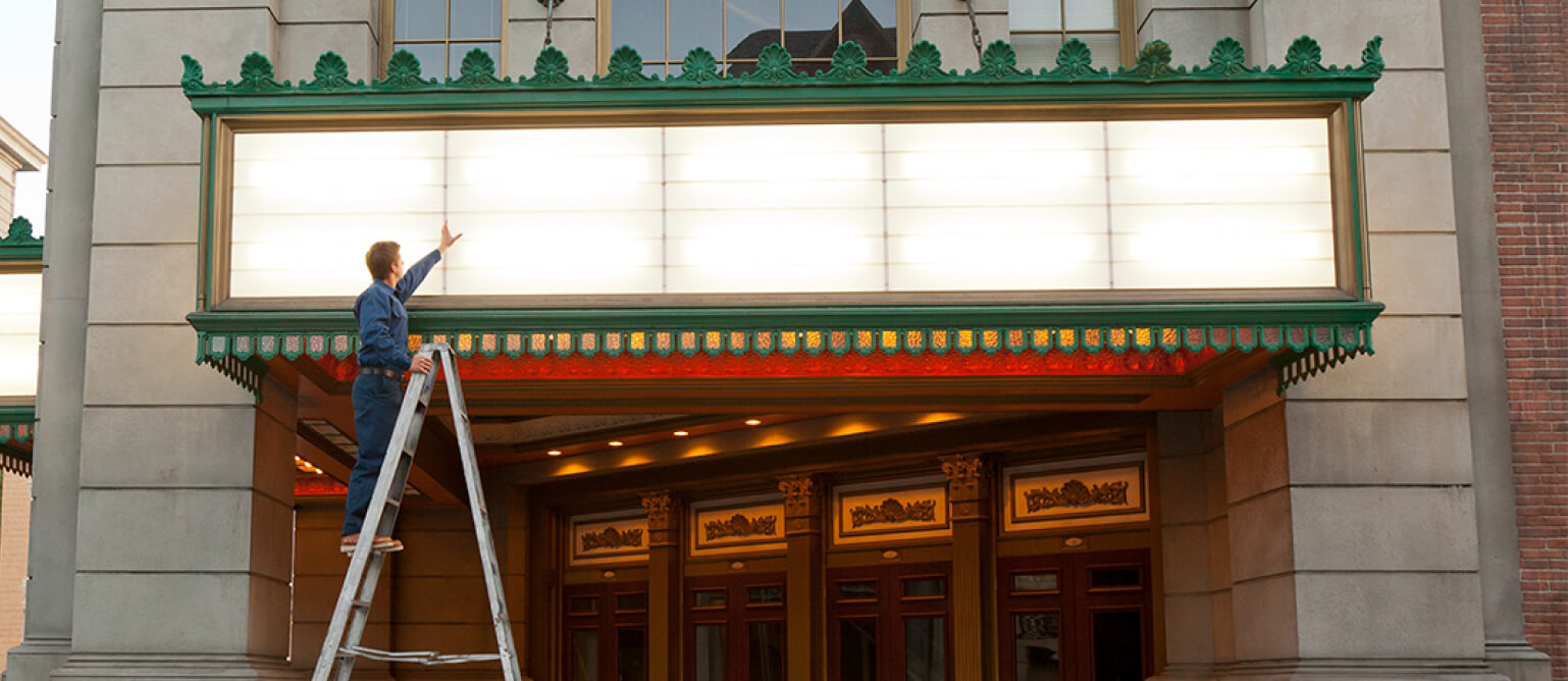 A repairman is repairing the light sign in front of the door.