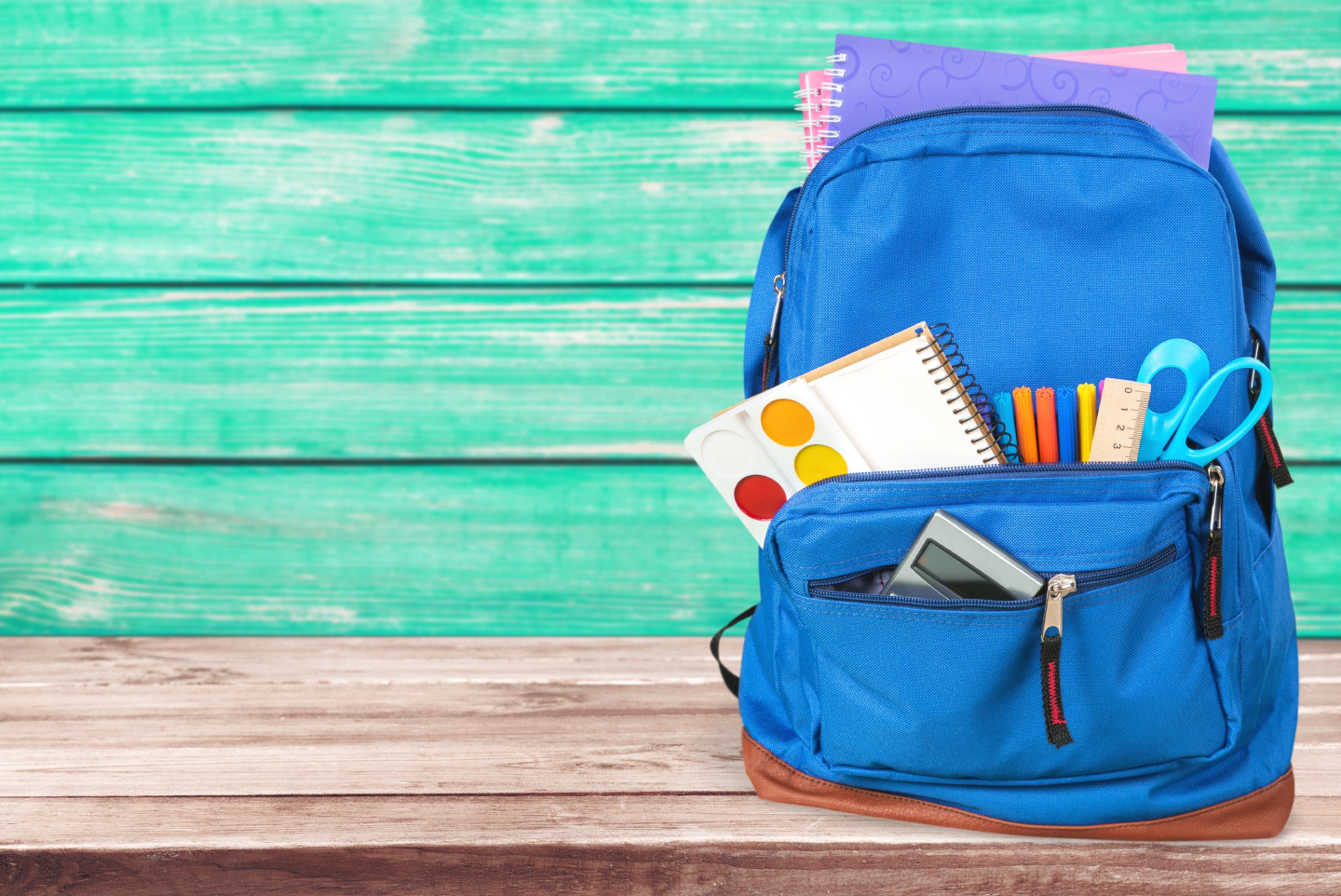 a blue backpack with school supplies sticking out of it sits on a wooden table