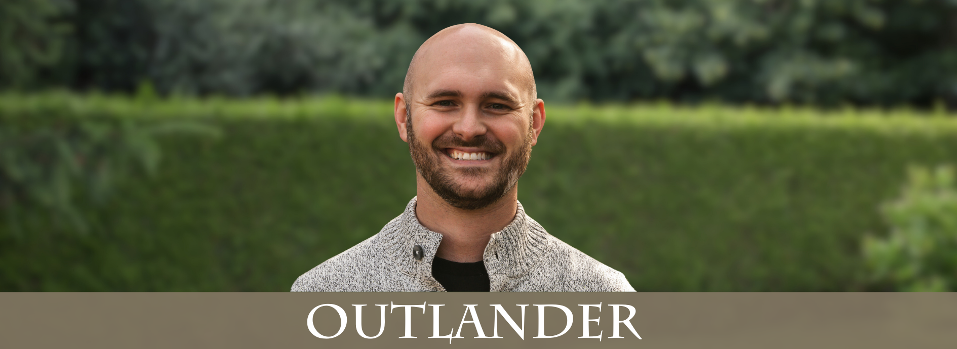young bald man with a beard, wearing a white marled sweater with buttons at the neck.