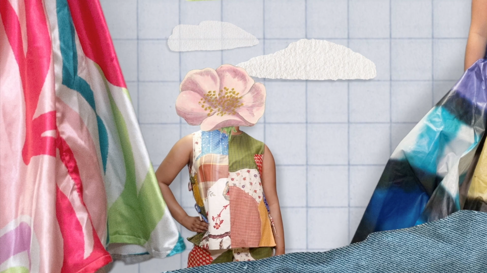 A person with a large pink flower for a head wears a sleeveless patchwork shirt and red polka-dot pants, standing in front of a light blue grid background with paper clouds. Colorful fabric and denim are visible on the sides and bottom of the frame.