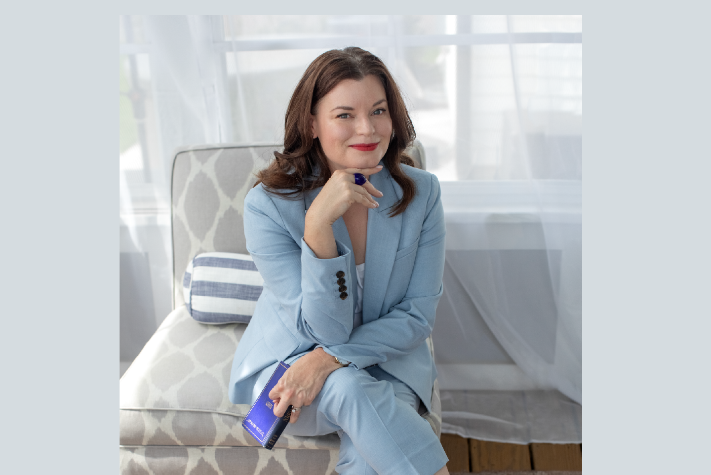 Brunette woman in blue pant suit  in blue room with legs crossed