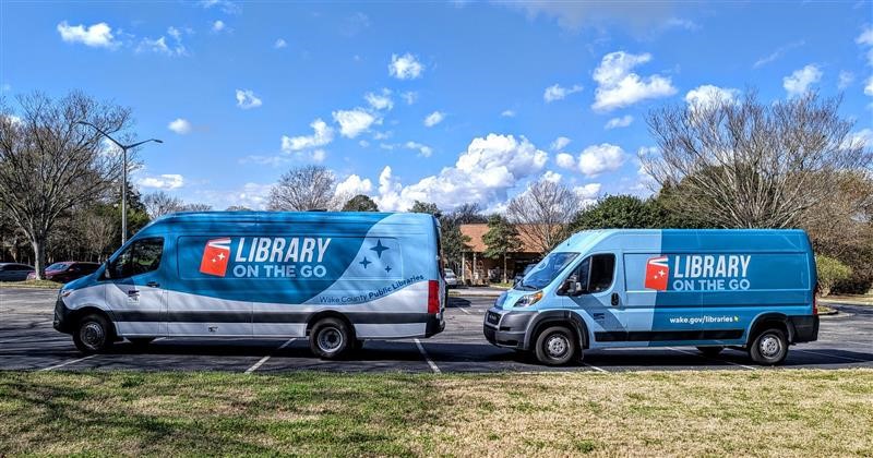 Two “Library on the Go” bookmobile vans parked side by side in a lot on a sunny day.