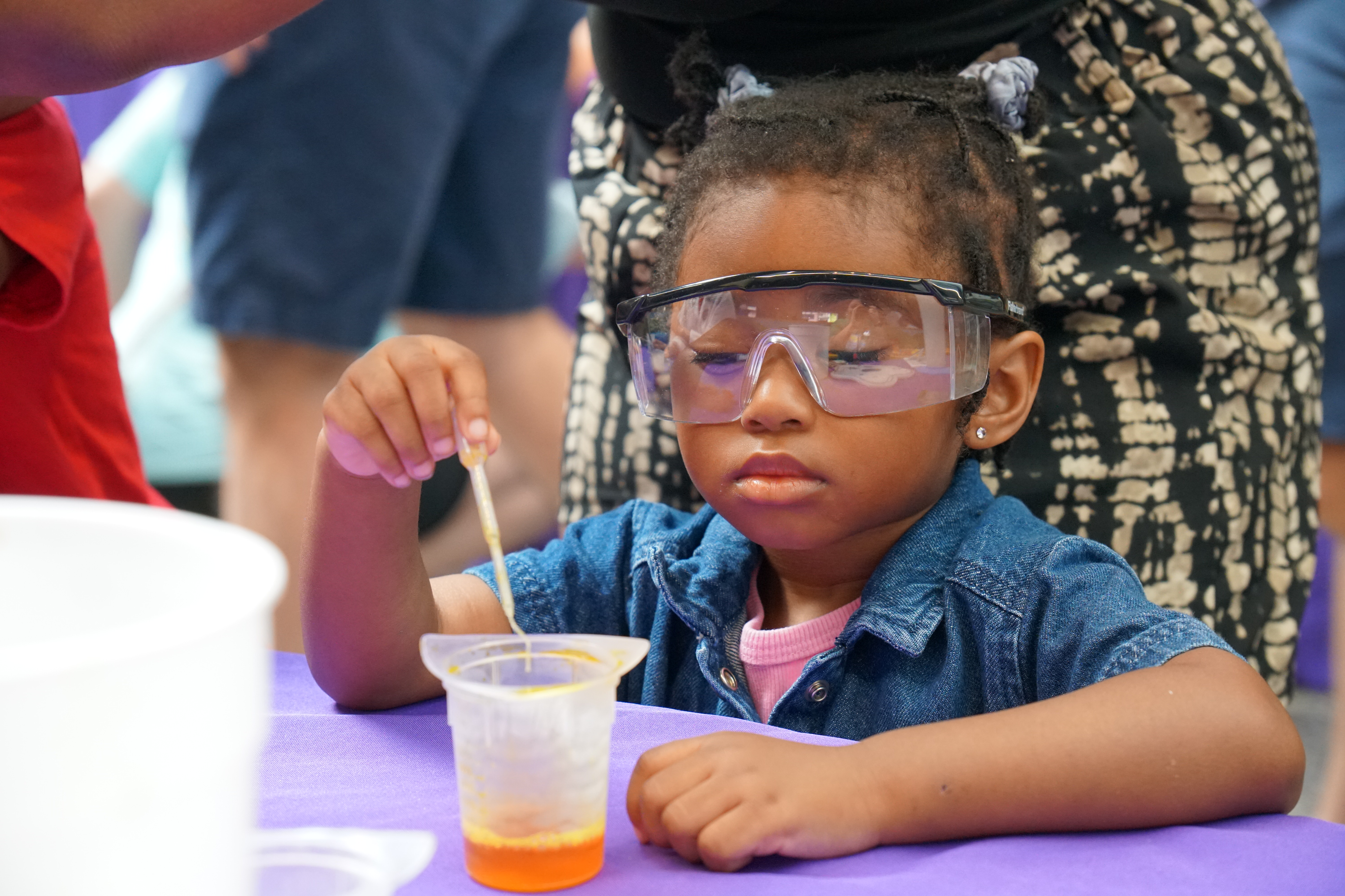 image of a young girl wearing safety goggles squeezing orange liquid from an eyedropper into a beaker