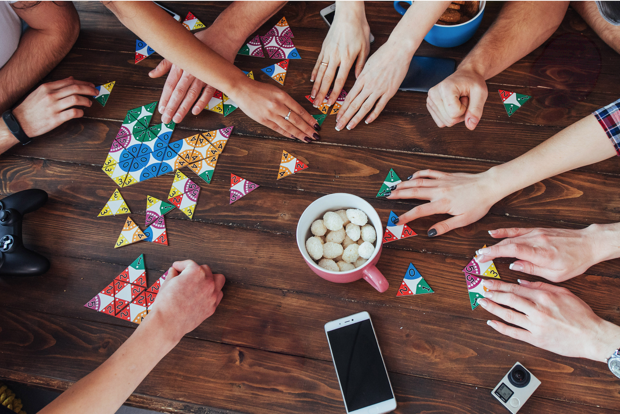 top down view of different hands playing a board game with snacks and a phone on the table
