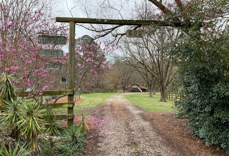 wooden archway entrance and path surrounded by trees and plants with barn in background
