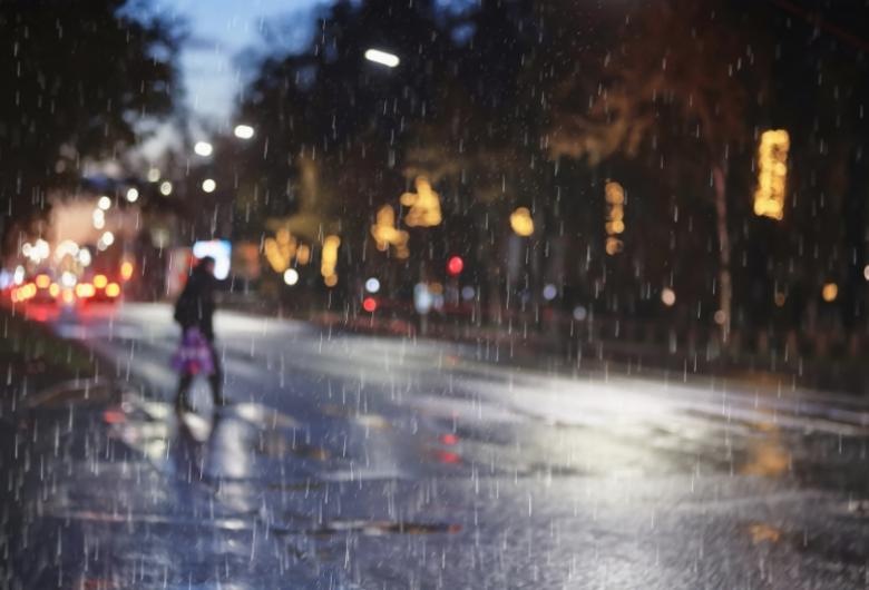person crosses a wet city street at night during rainfall