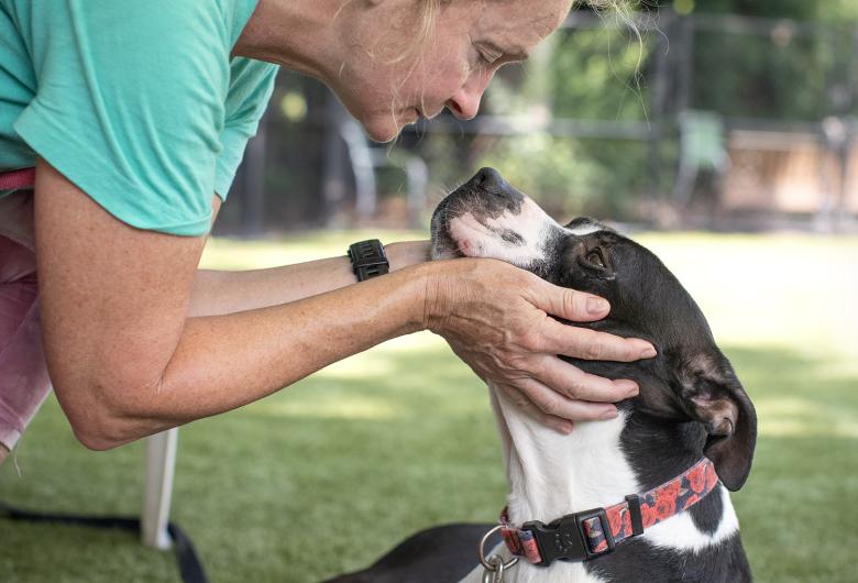 Christine kneels to connect nose-to-nose with a black-and-white dog in the play yard.