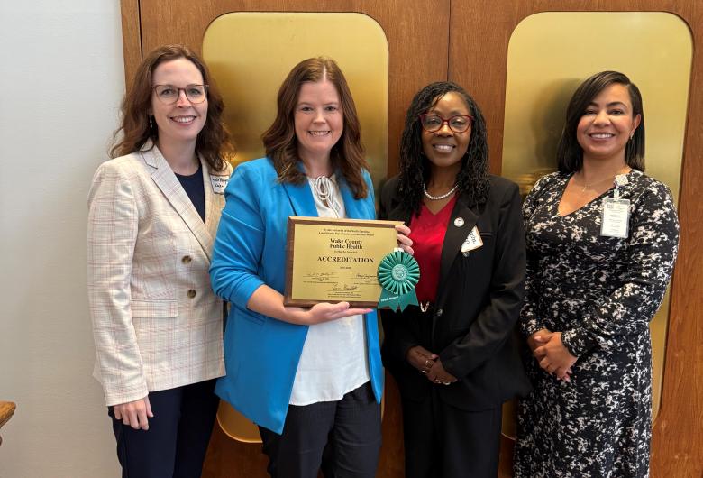 Four women standing together indoors, smiling, with one holding an accreditation plaque.