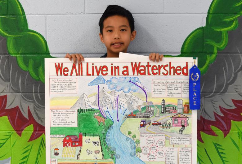 smiling child holds watershed poster