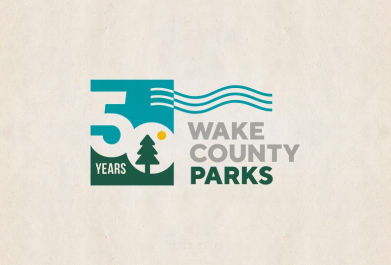 Wake County Parks 50th anniversary logo featuring a large “50 Years” with a tree and sun icon, and the words “Wake County Parks” alongside stylized wave lines.