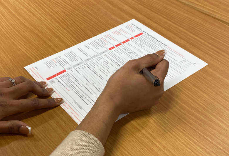 Hands filling out a voter registration form on a wooden table.