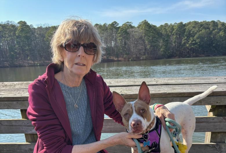 Wake County foster Kim Leon sitting on a dock with a foster dog on leash beside a lake.