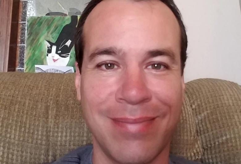 Close-up of a man smiling while sitting on a couch indoors.