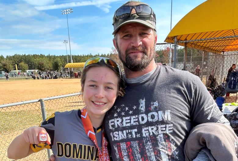 Softball player wearing a medal posing with an adult on a field.