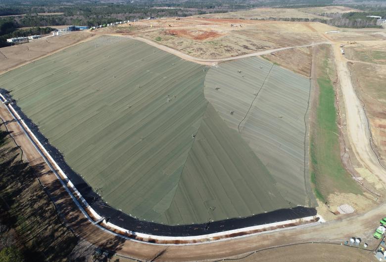 Aerial view of a landfill with a large completed interim cover, surrounded by dirt roads and open land.