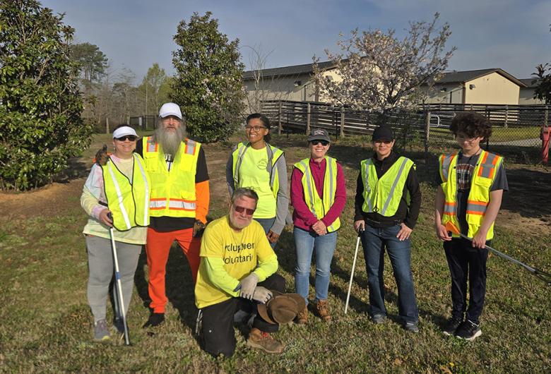 Group of volunteers in safety vests pose outdoors with litter pickers during a community cleanup event.