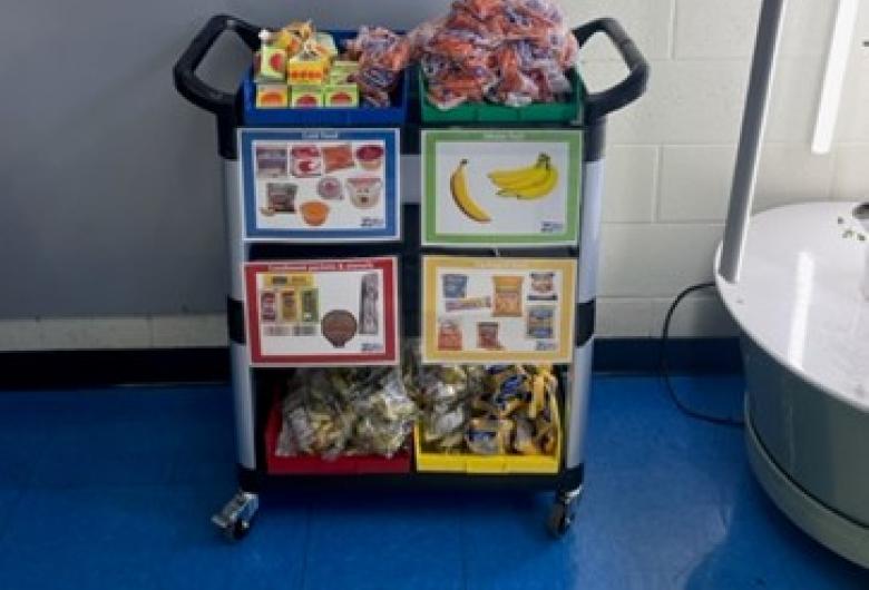 School SHARE cart with fruit and packaged snacks beneath a poster encouraging students to share uneaten food.
