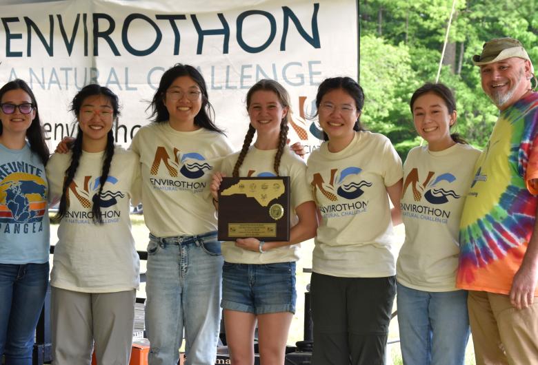 Group of students and adults posing with an award plaque in front of an Envirothon Natural Challenge banner.