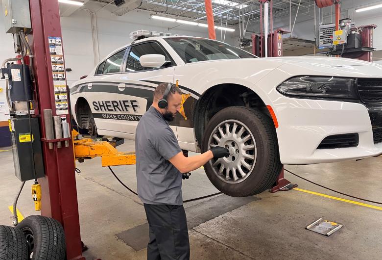 Technician servicing a Wake County Sheriff patrol car on a lift inside a maintenance shop.