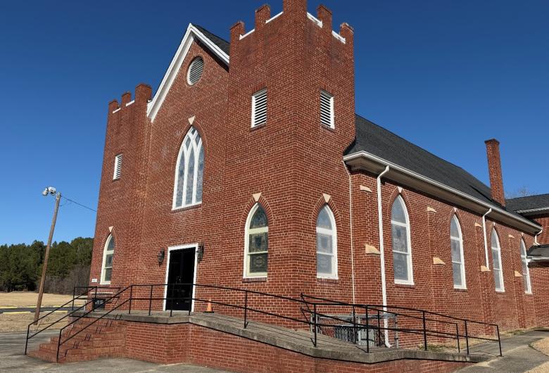 Red brick church with arched windows and a ramped entrance under a clear blue sky.