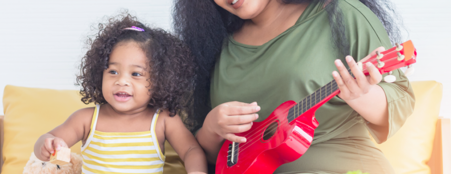 Woman and child sitting on couch. Woman is playing red guitar.