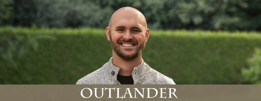 young bald man with a beard, wearing a white marled sweater with buttons at the neck.