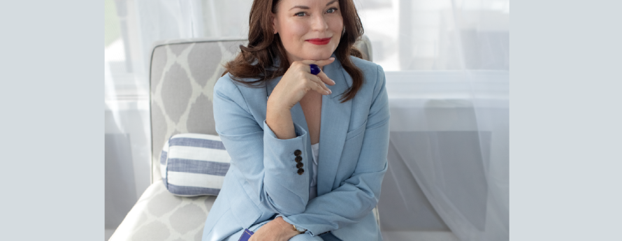 Brunette woman in blue pant suit  in blue room with legs crossed
