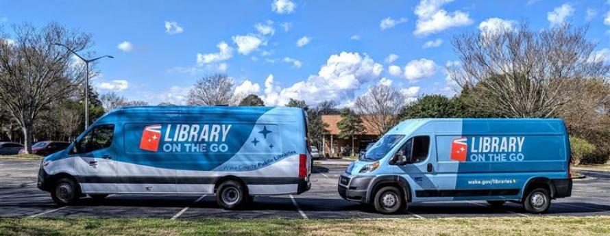 Two “Library on the Go” bookmobile vans parked side by side in a lot on a sunny day.