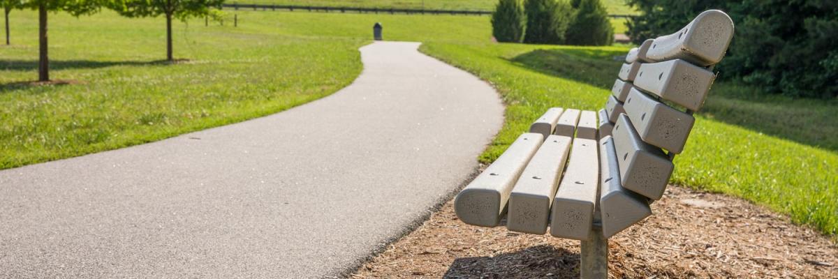 A paved trail running past a park bench with grassy slopes in the background.