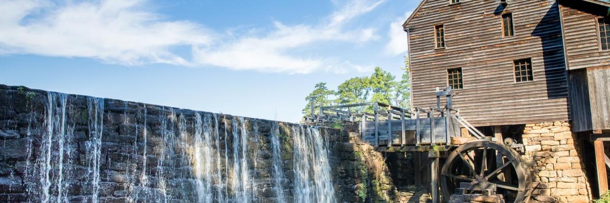 View of historic old wooden mill building beside dam with waterfall