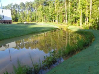 A landscaped stormwater pond beside a commercial building on a sunny day.