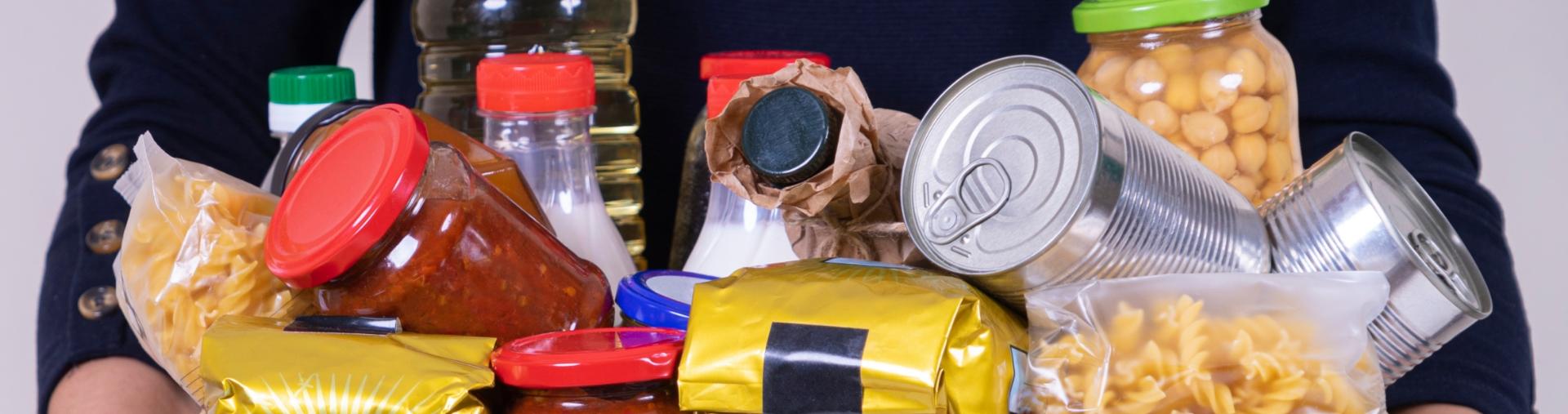 person holding armload of cans, bags and jars of food