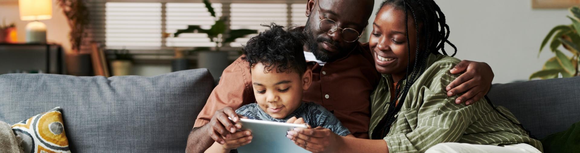Family sitting together on a couch, smiling while looking at a tablet.