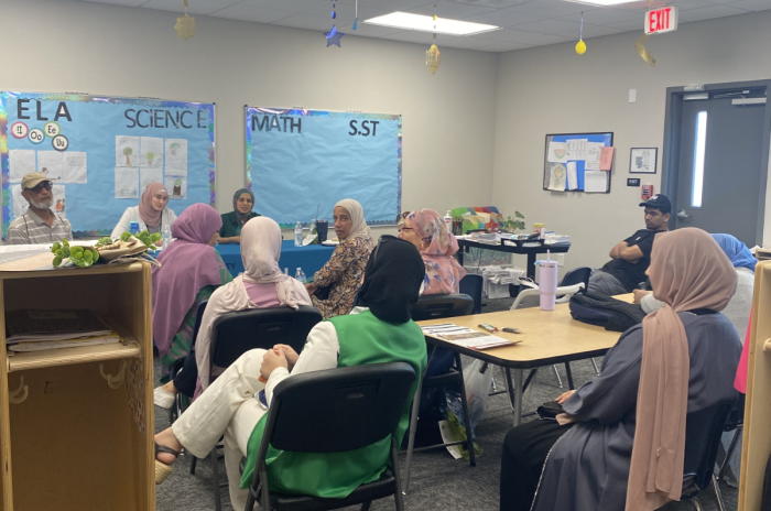 A classroom scene featuring a group of individuals seated in chairs, focused on the instructor or presentation.