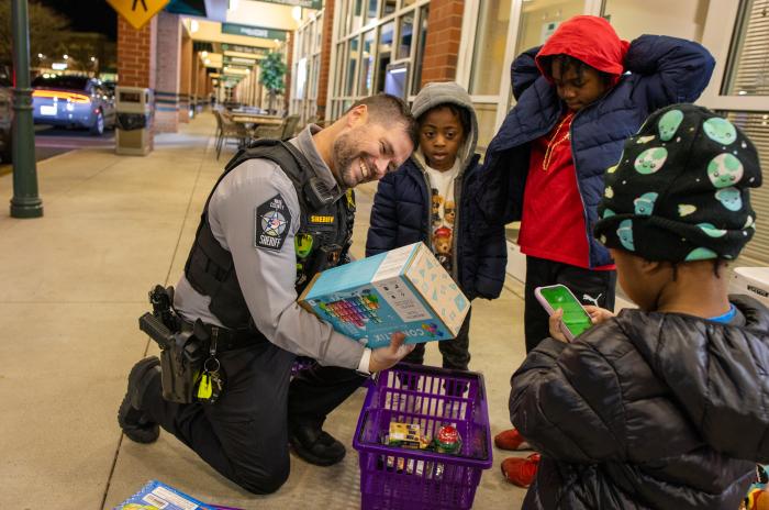 A deputy looking at a toy as a group of kids stands around him