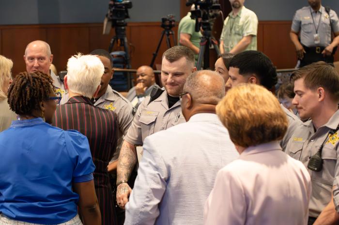The six deputies are lined up as the County Commissioners shake each of their hands at the meeting. 