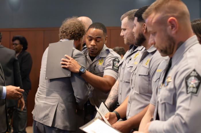 A line of deputies and one of them is giving a hug to Adam Levy while holding his certificate. 