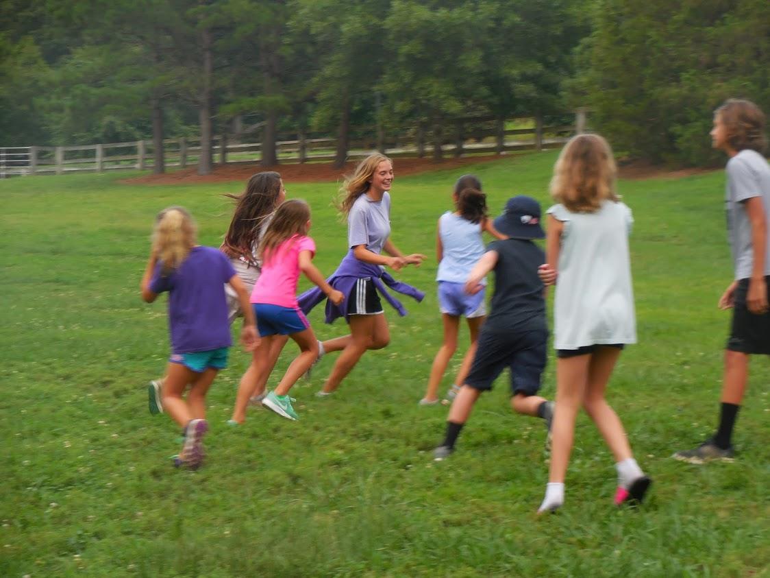 Group of children run and play tag in grassy field