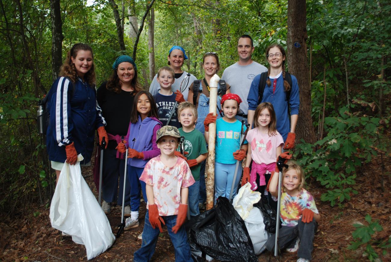 group of volunteers stand in forest with trash bags