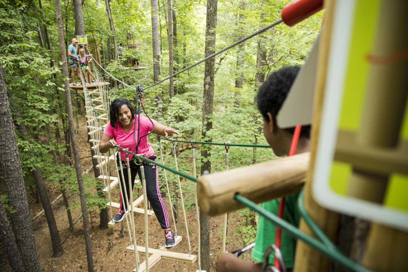 a woman in a hot pink top crossing an elevated obstacle on a Go Ape course