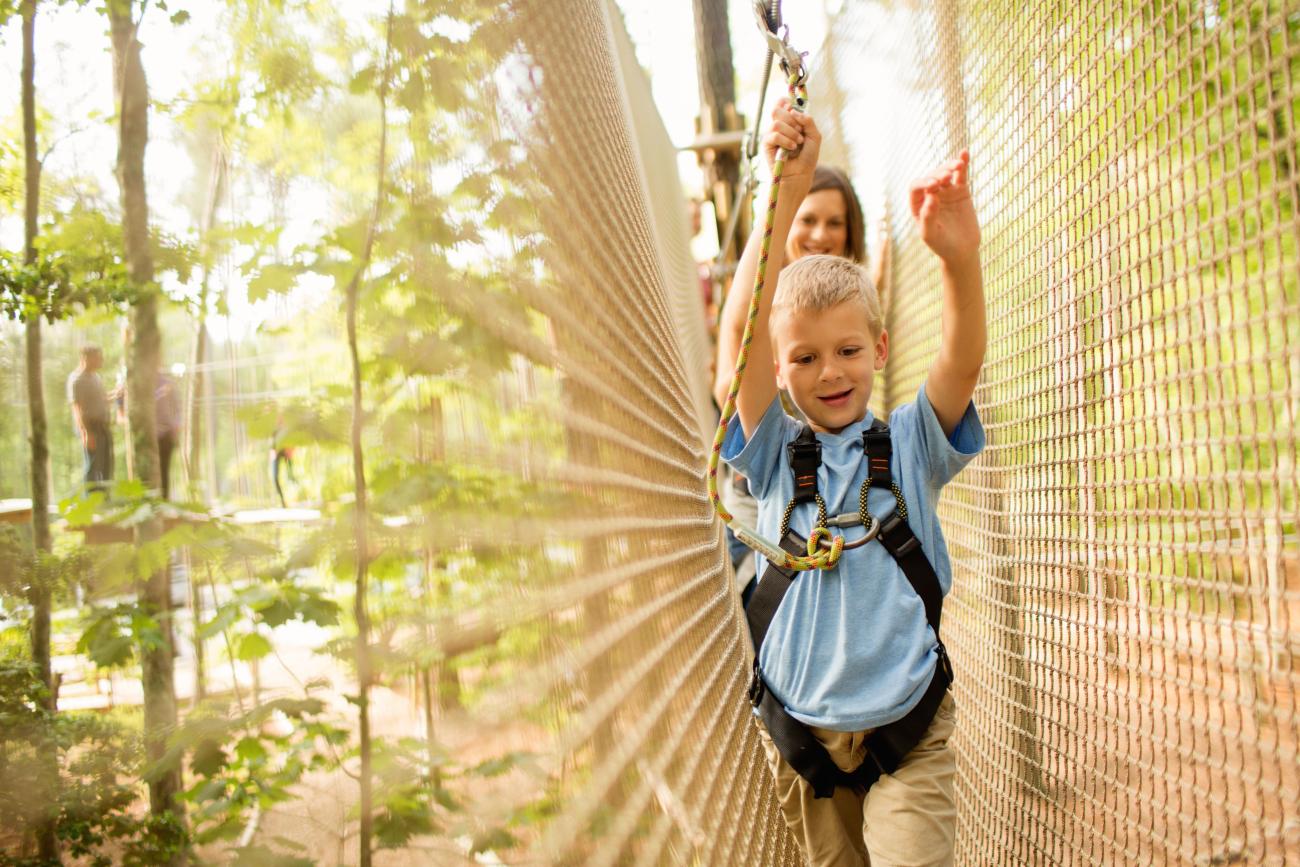 Young boy navigating an aerial obstacle with net walls on each side of him on the Go Ape Journeys course