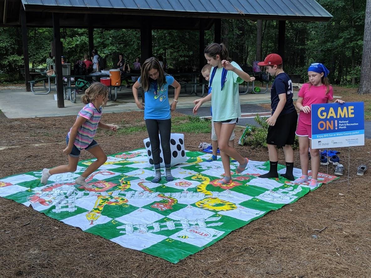 Group of kids playing "Snakes and Ladders" jumbo game on a large play mat