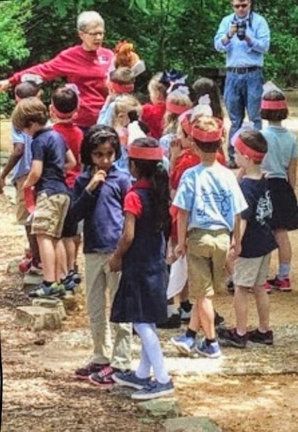 Tour guide leads group of children down dirt path to mill.