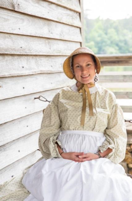 Woman sits in chair by mill in historical outfit