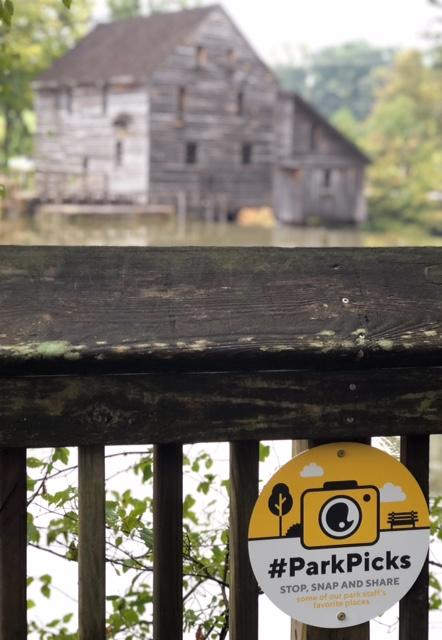 metal sign on wooden boardwalk with mill and pond in background