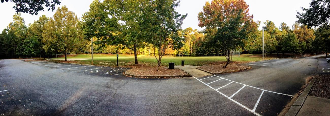 image of open play field with volleyball net, with surrounding trees and parking lot