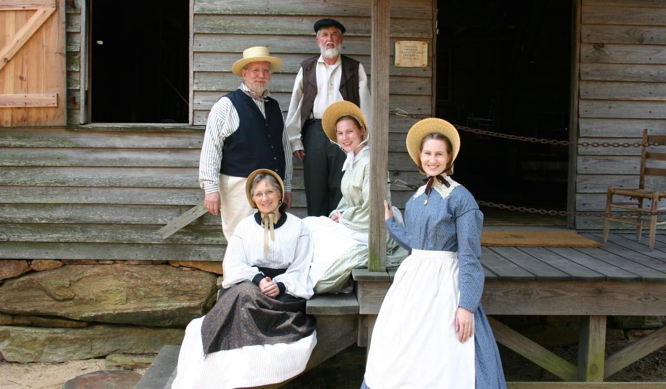 Group of costumed volunteers stand together in front of old wooden mill