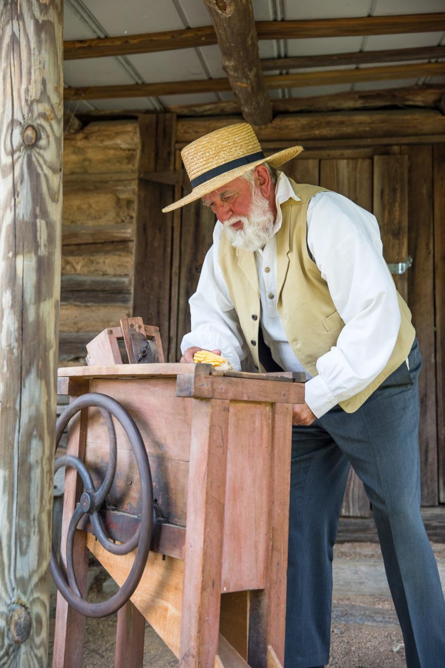 Costumed interpreter grinds corn inside of historic mill building