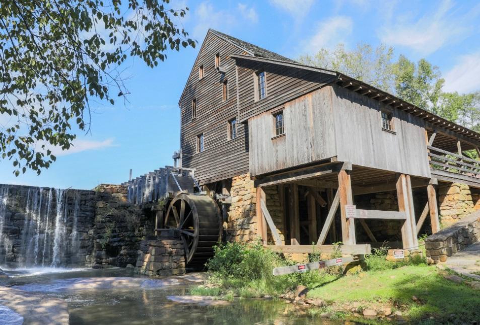 View of old wooden mill building with water flowing over dam