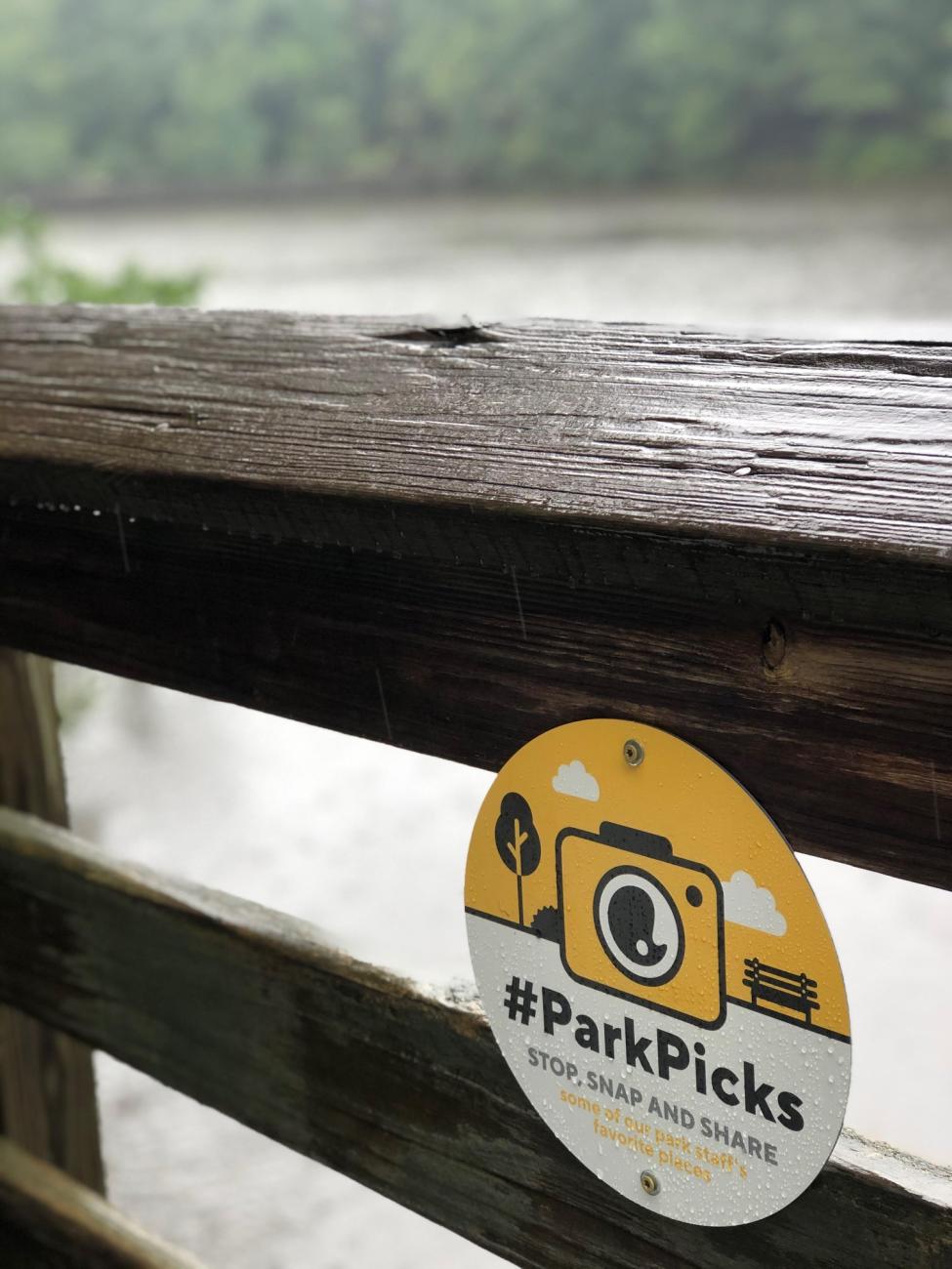 image of pond in the background and wooden railing with sign on it